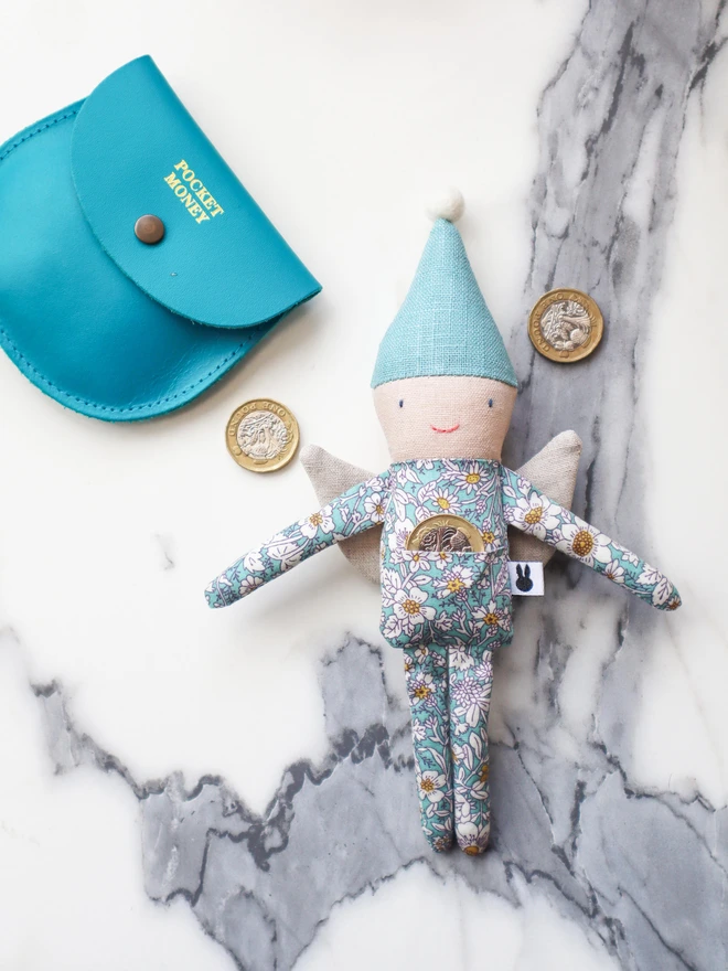 Handmade fairy doll with light blue floral outfit and light blue pointy hat with cream pompom on top. A pound coin in its pocket.