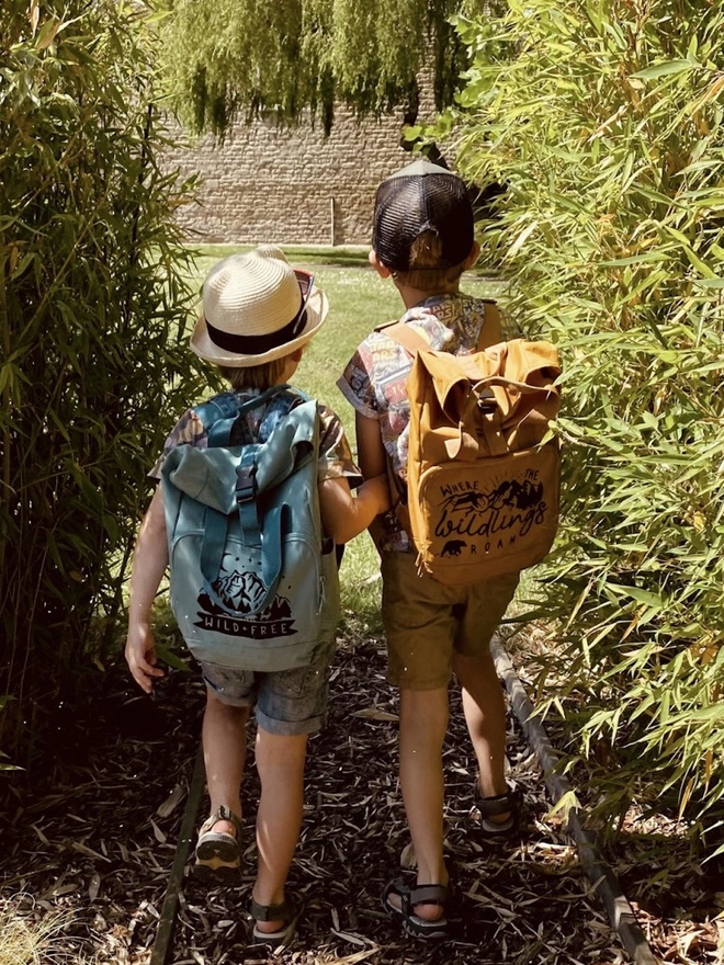 'Wildings' Children’s Recycled Roll Top Back Pack, two children outdoors wearing a colourful backpack. 