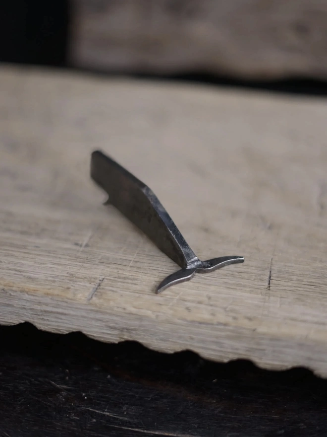 Whale Bottle Opener, a whale shaped bottle opener sitting on a wooden surface. 
