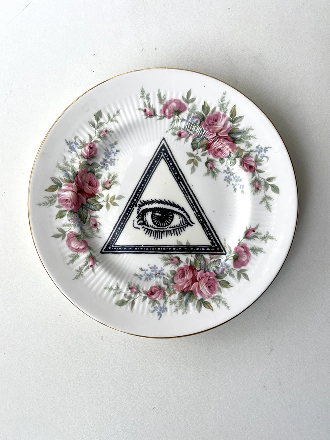 a vintage plate with a floral border of pink flowers, in the centre is printed a vintage illustration of an eye