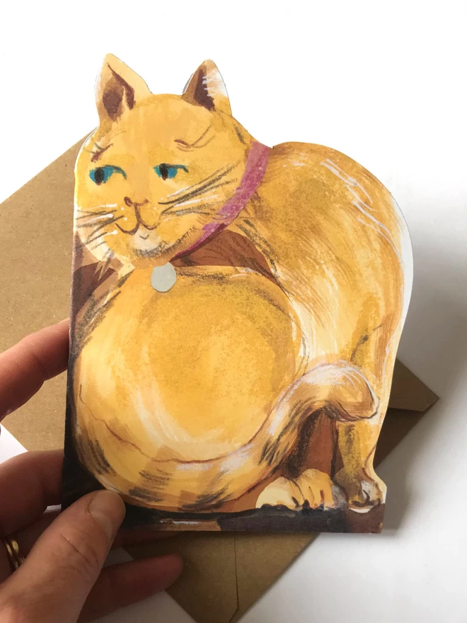 Hand holds shaped greetings card showing mustard yellow cat