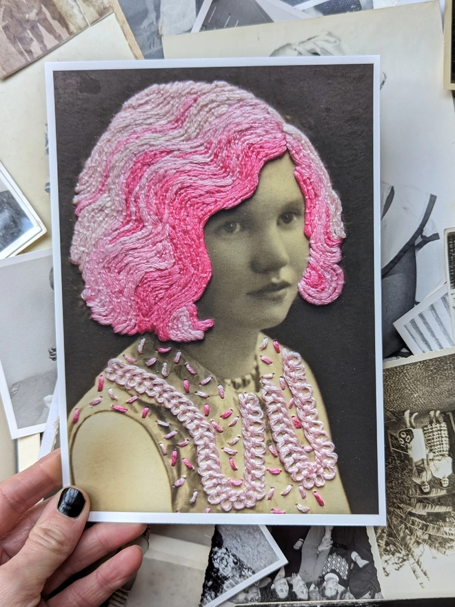 Print of B&W girl, with embroidered pink hair and dress, held over photos
