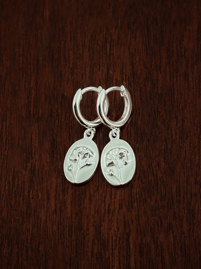 Sterling Silver Huggie drop earring with forget me not charms charms on a dark background representing memories in the language of flowers