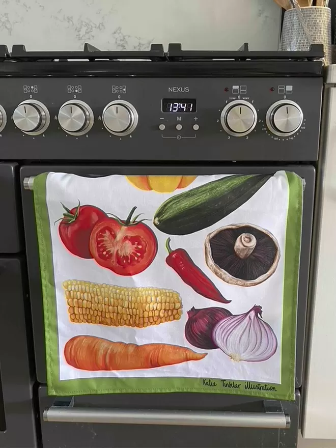 A vegetable themed tea towel hanging on a cooker