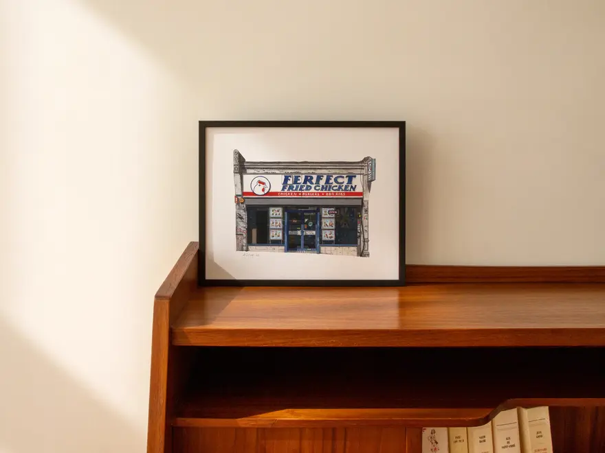 Forest Hill Ferfect Fried Chicken Shop Giclée Print , a print of a fried chicken shop in a black frame on a wooden surface against a white backdrop. 