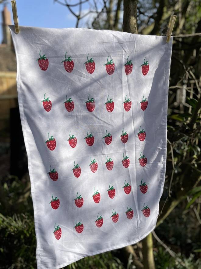 Kitchen tea towel with a strawberry pattern displayed outdoors in natural light.