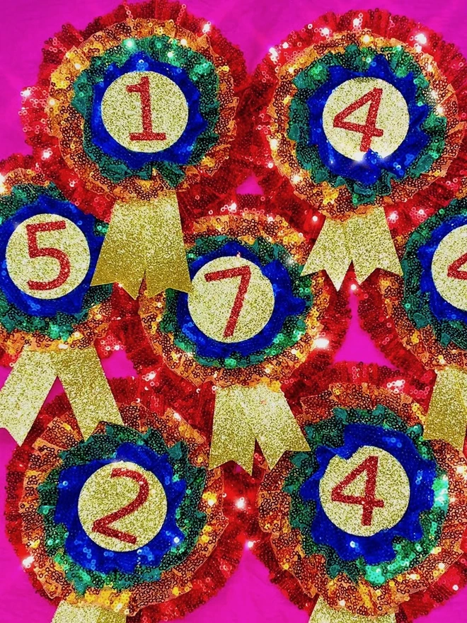 A selection of seven rainbow birthday rosettes ranging from ages one to seven. They are arranged in rows against a pink backdrop.