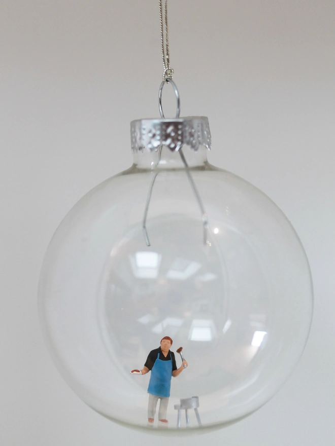 Miniature figure of man barbecuing in a glass Christmas bauble