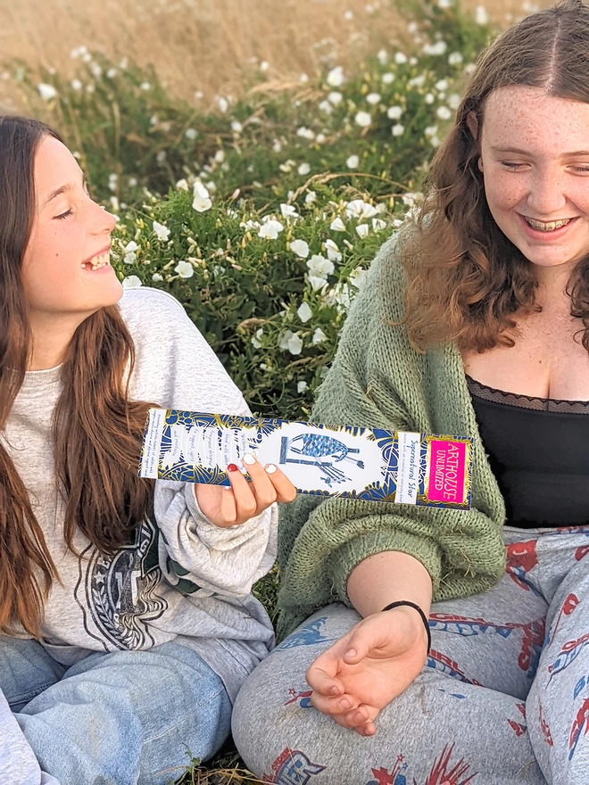 2 girls in a field holding supernatural star well being charity incense sticks with blue illustrations