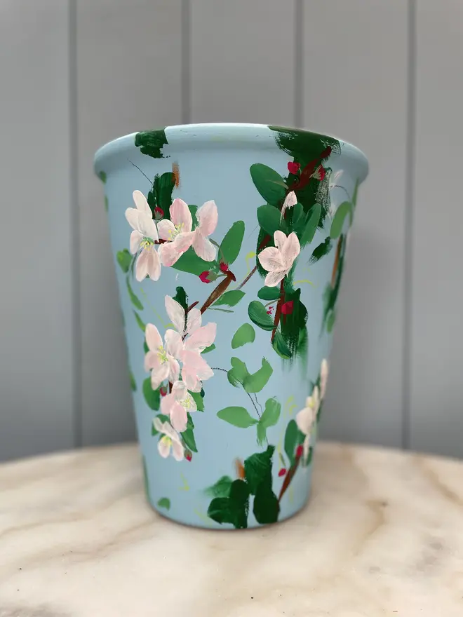 Unique hand-painted terracotta pot featuring apple blossoms on a pale blue background  