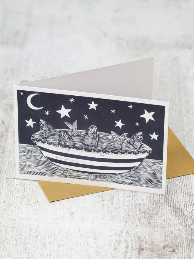 Greeting Card with an image of a Fish Pie in a stripey dish, with the fish gazing up at the stars in the sky, taken from an original lino print