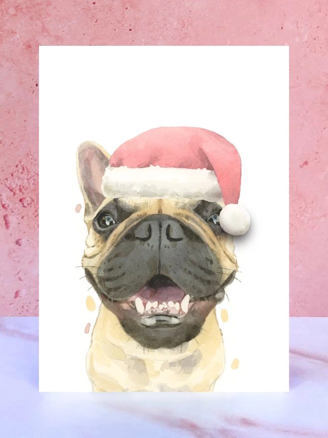 A Christmas card featuring a hand painted design of a frenchie, stood upright on a marble surface. 