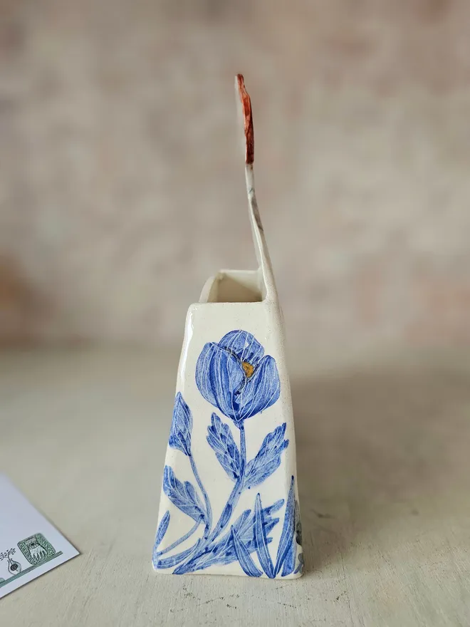 a large vase shaped like a lady with red hair looking up with blue flowers painted on her dress, side view