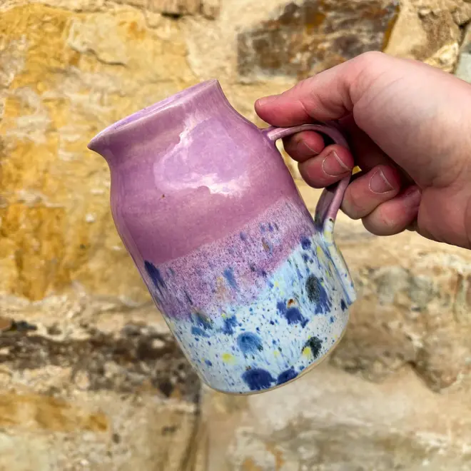 Shoreline Medium Jug, a colourful jug being poured against a brick wall backdrop. 