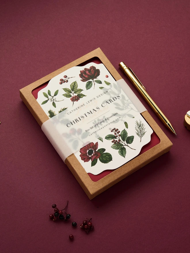 Box of 8 cards, with red envelopes. gold foil and die-cut shape cards with greens and red botanicals
