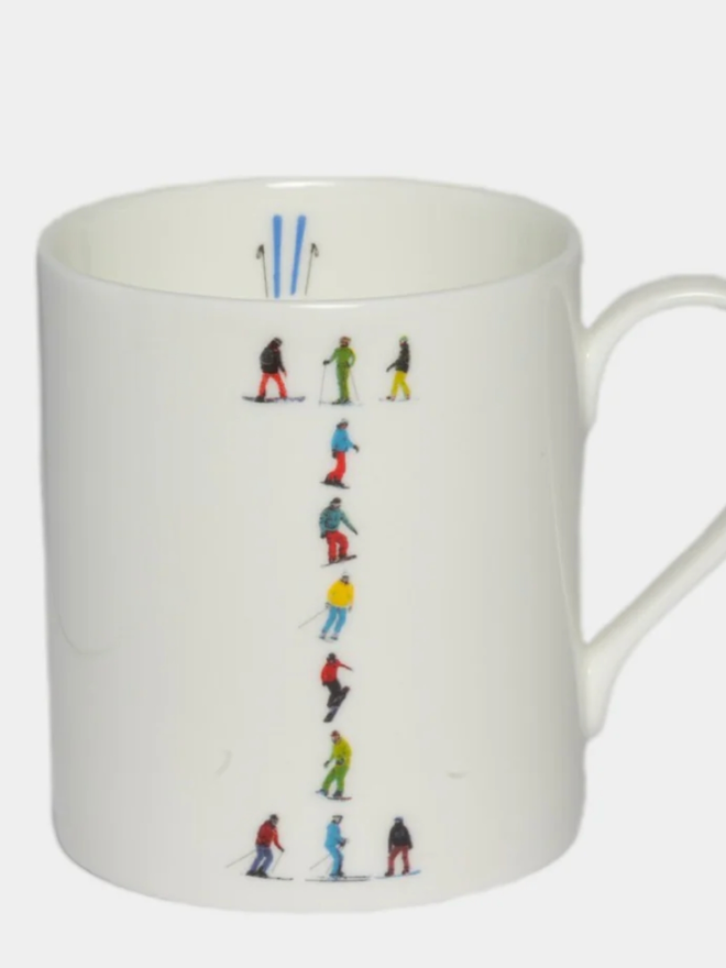 A simple white mug illustrated with an ‘I’ made of small, multicoloured skiers. The mug is set against a plain, white background.