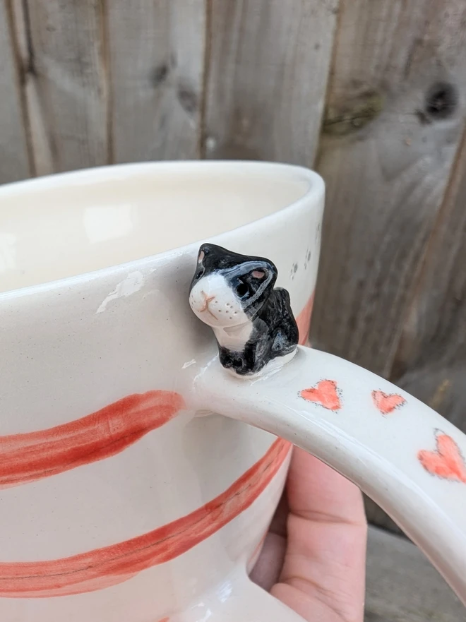 pottery cup with red stripes, hearts and a ceramic black and white cat on the handle