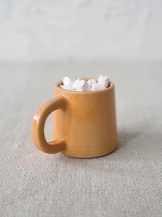 Classic Ceramic Espresso Mug, a colourful ceramic espresso mug sitting on a plain surface against a white backdrop. It is accompanied by a group of marshmallows. 