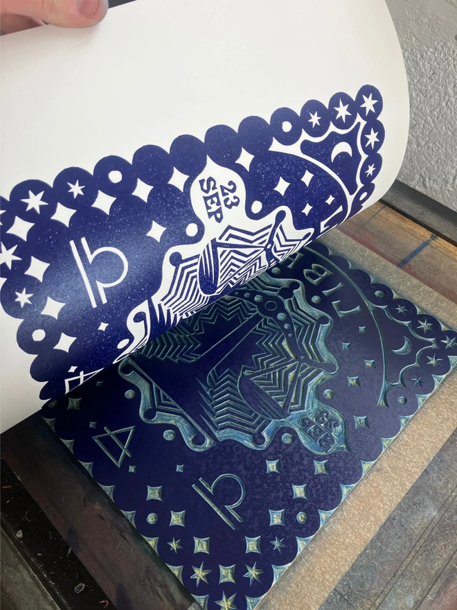 libra zodiac linocut. a linocut set of scales and zodiac symbols printed on a blue background.