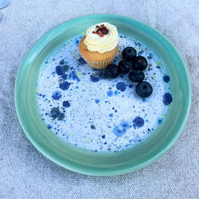 Shoreline Side Plate, a colourful plate placed on a stone surface. It is accompanied by fruits and a sweet treat. 