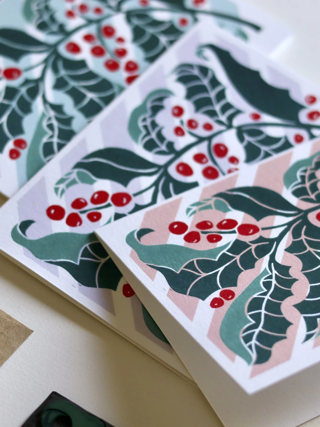 linocut holly leaves greeting card on a candy striped back ground in a pack of 4