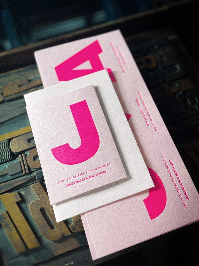 Bespoke Amour concertina wedding invitation unfolded to reveal oversized initials, heart motif and personalised wedding details, hand printed in fluorescent pink on luxury Candy Pink card with Pristine White envelope..
