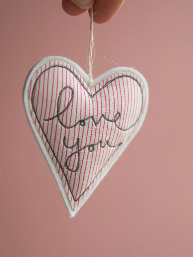 Love you embroidered Valentine's Day heart. A heart shaped hanging decoration in a red striped fabric with the words I love you embroidered on the front.