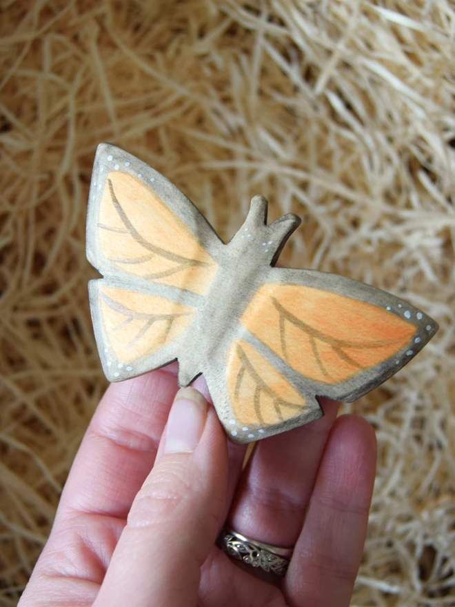 wooden monarch butterfly held in hand above woodwool