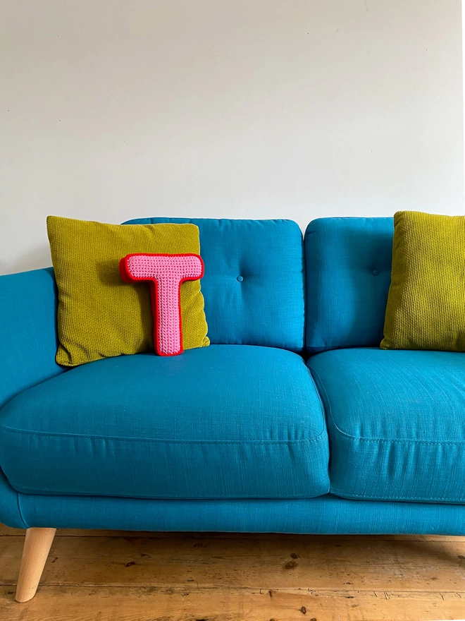 Crocheted Letter T in Bubblegum Pink and Postbox Red, on a turquoise sofa