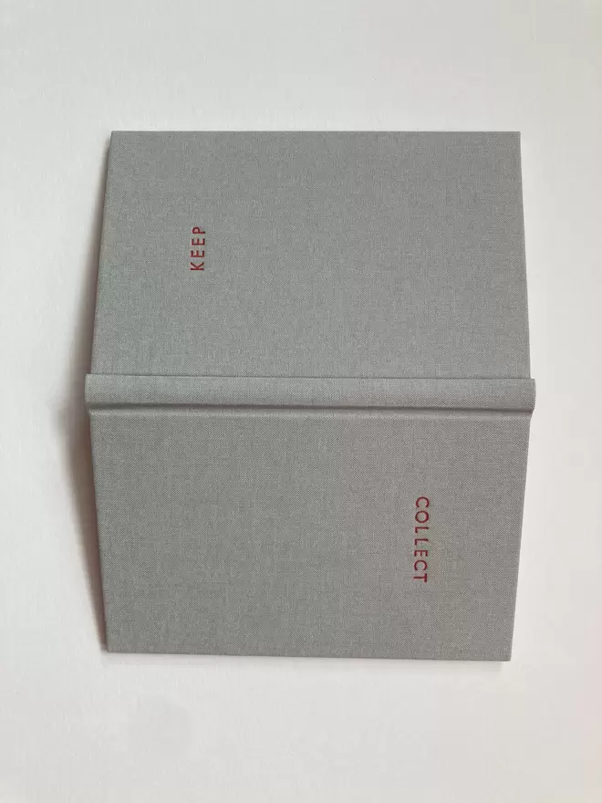 An open handmade pocket sized notebook in dove grey cloth with bespoke lettering in red foil
