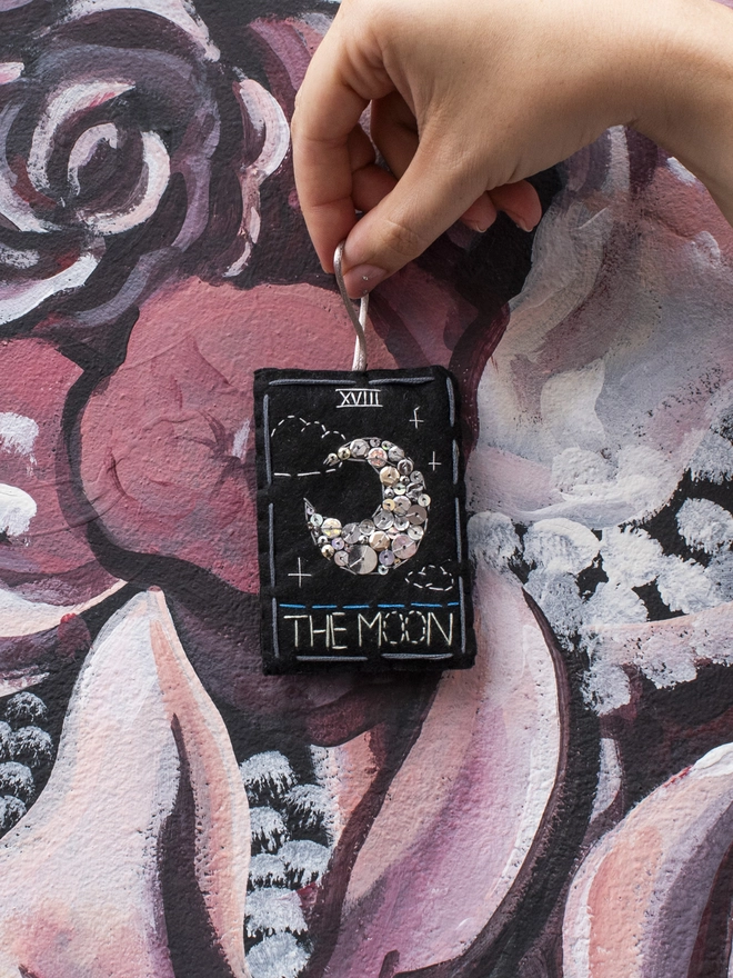 A handcrafted felt ornament with sequins and embroidery depicting "The Moon" tarot card. 