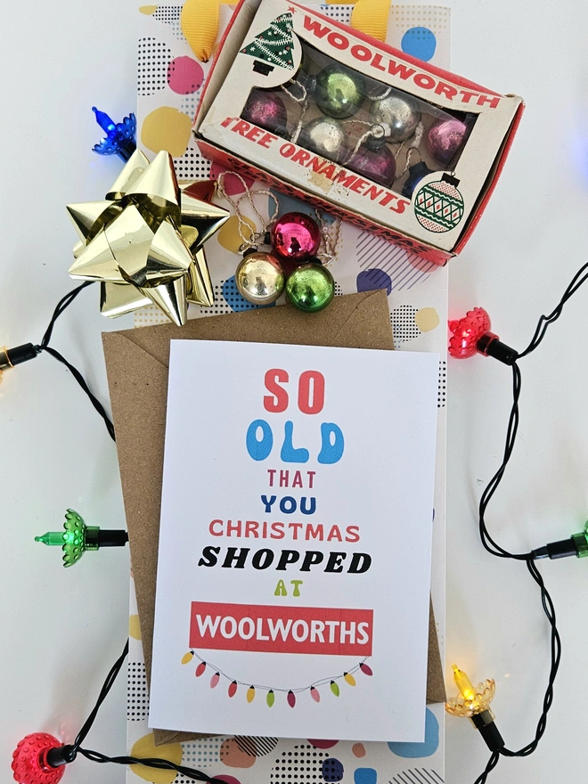 A photograph of the front of a humorous A6 greeting card illustrated using brightly coloured text and the retro shop logo. The text says so old you Christmas shopped at Woolworths with string lights