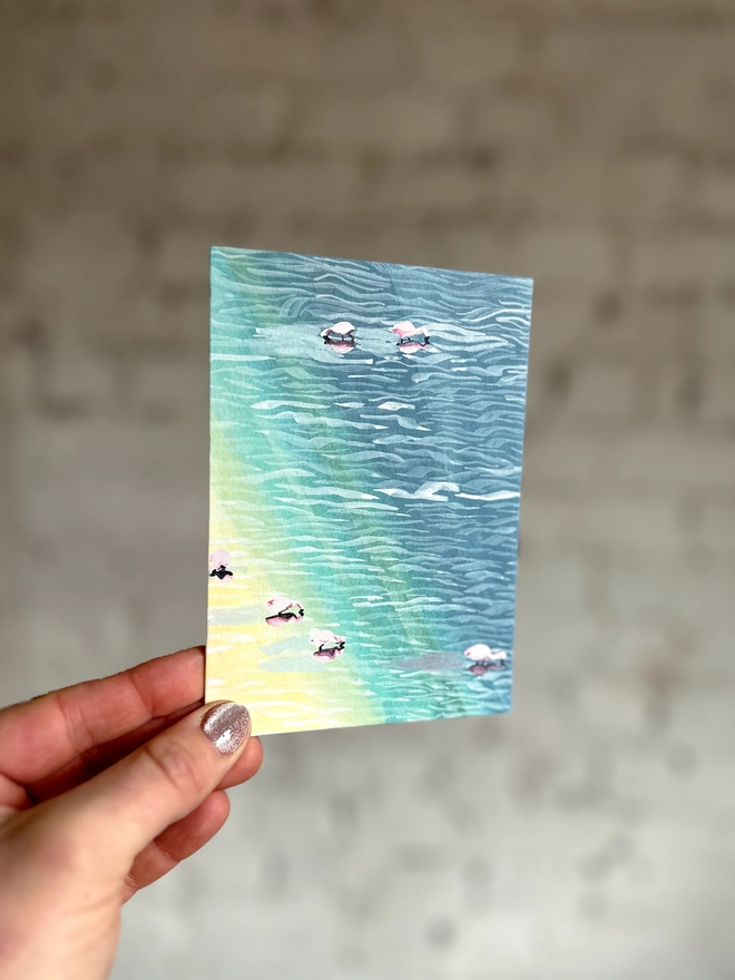 a greetings card featuring an illustration of flamingos in water with a rainbow reflection