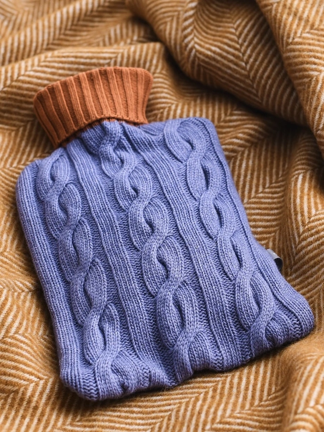 Cashmere Hot Water Bottle Cover, a colourful water bottle sitting on a blanket. 
