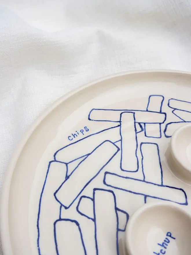 Dippy Chips & Nuggets Dinner Plate, a white dip dinner plate with blue outlines for nuggets and chips sitting on a white bed cloth. 