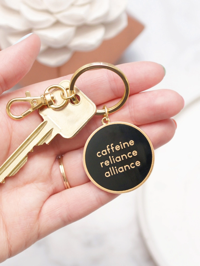 Hand holding a Caffeine reliance alliance enamel keyring with key attached