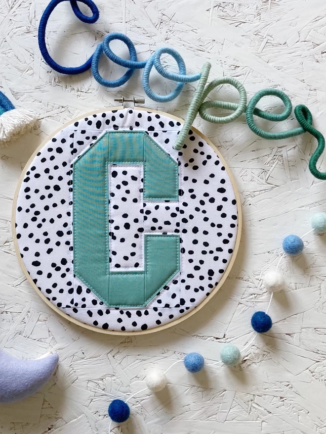 Personalised quilted hoop seen against a spotted background with the letter 'C' in blue.