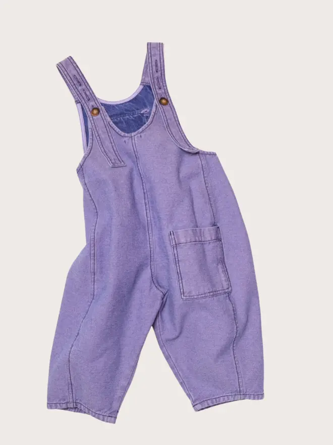 Back flat lay of Studio Koter Kai dungarees in Lilac Overdye, showing the flap patch pocket and seamed leg.