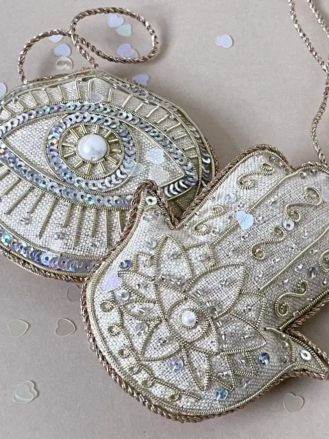 evil eye and hamsa hand embroidered decoration. silver beaded hanging decorations photographed together on fabric cushion background.