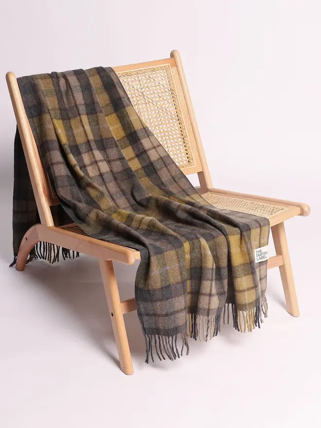 Buchanan Natural Recycled Wool Blanket, a yellow and brown blanket draped over a wooden chair on a white surface against a plain backdrop. 
