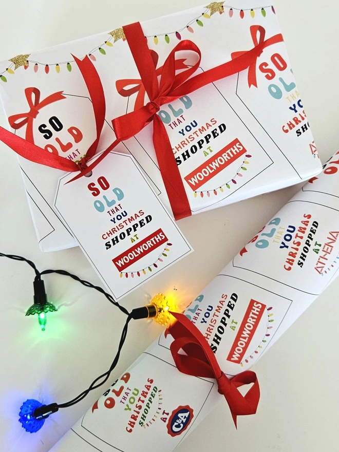 A photograph of a present wrapped in paper that has tags with a red bow printed on it. On each tag it says so old that you Christmas shopped at Woolworths, Athena, C&A, Tie Rack, Sock Shop illustrated using brightly coloured text and the retro shop logo. The tag on the present says so old that you Christmas shopped at Woolworths to match the paper.