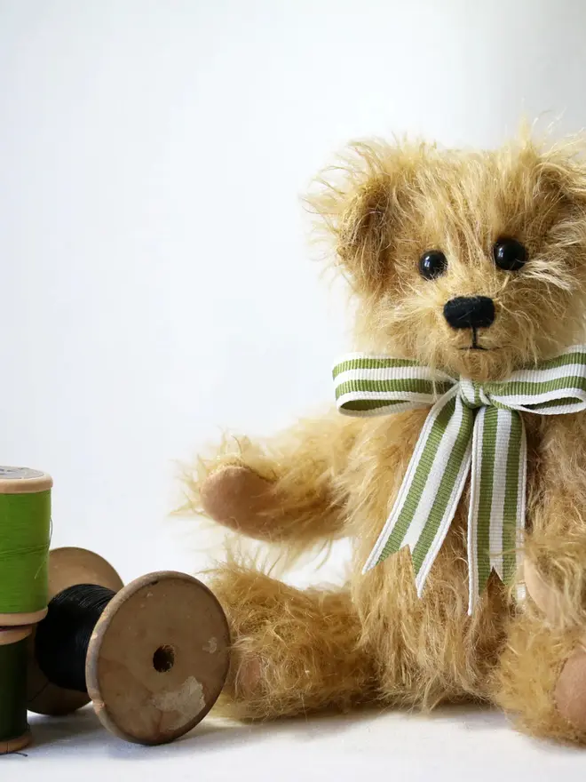 Handmade brown teddy bear sitting upright with a green striped ribbon bow against a plain background.