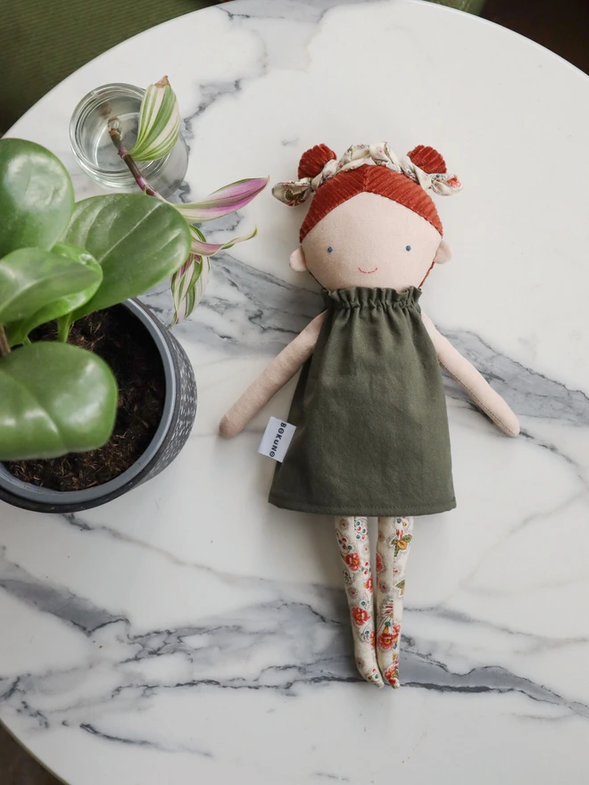 Handmade linen doll with light skin wearing dark green cotton dress and cream floral bows and tights. It has braided red hair made with corduroy.