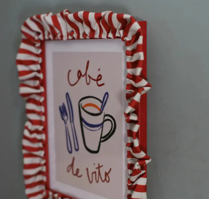 Soft ruffle frame with red and white striped fabric trim hanging on a grey wall. 
