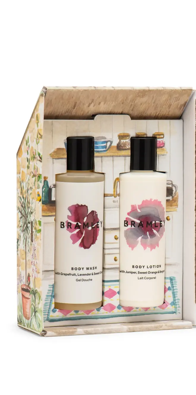 interior of cardboard cottage, holding two bottles of product, one body wash and one body lotion, both with white and pink labels and black lids