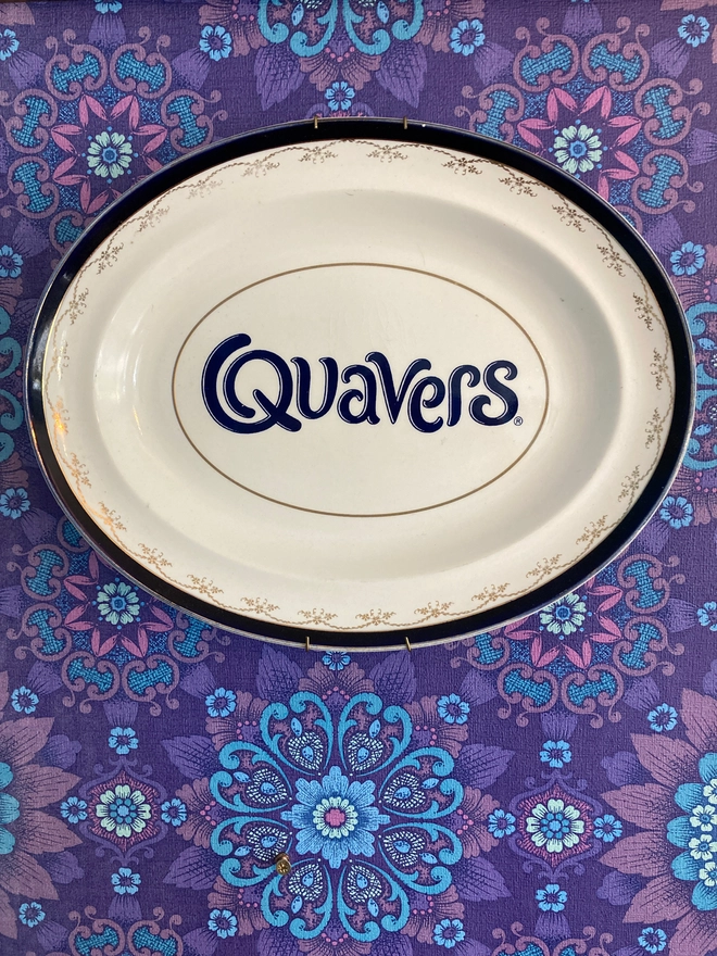 oval vintage china plate with a navy rim, featuring a navy blue 'Quavers' logo across the centre.