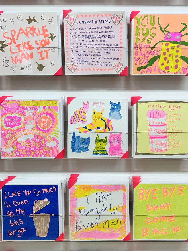 A cat card with fluro pink blue & yellow cats with curious stares & funny poses on a rack 
