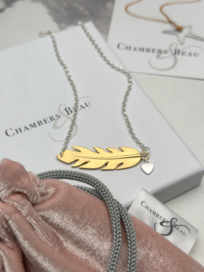 sterling silver chain with gold horizontal feather charm. a small silver heart charm hangs from the chain next to the feather