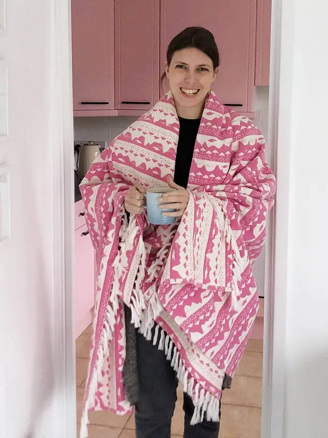 Pink Belle Mare Woven Throw, a woman wrapped in a pink throw standing in a doorway. 