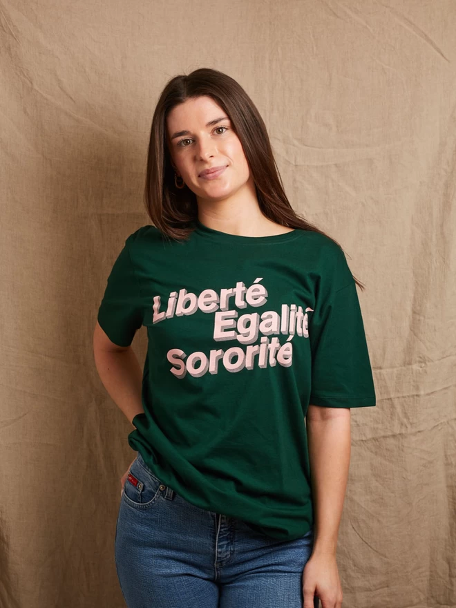Model is wearing a forest green cotton t-shirt with the slogan Liberté, Egalité, Sororité in pale pink written on the front